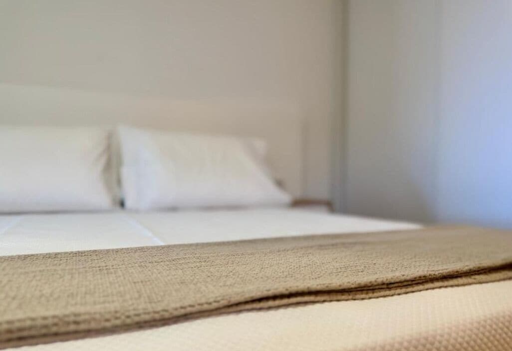 A bed with white linens and a beige blanket.