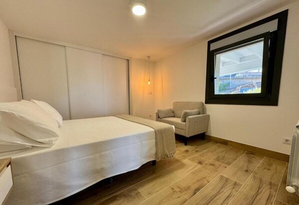 A bedroom with a bed, a chair, a window, and a radiator.