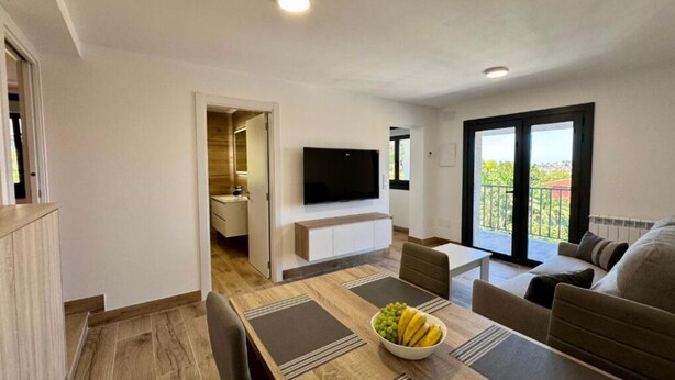A modern living room with a dining area, a flat-screen TV, and a balcony with a view. - Cíes Suitel Prado (Nigrán)