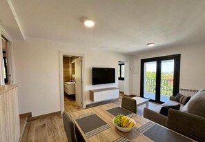 A modern living room with a dining area, a flat-screen TV, and a balcony with a view.