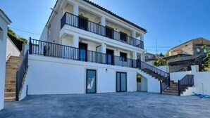 A two-story residential building with a balcony on the upper floor, a staircase leading to the entrance, and a flat roof. - Cíes Suitel Prado (Nigrán)