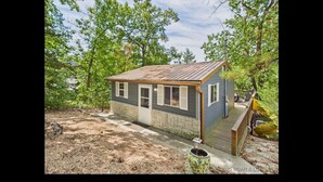 A small, single-story house with a sloped roof, a front porch, and a small deck. - Cozy Lake House with a Private dock and beautiful outdoor space. (Rocky Mount)