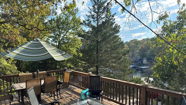 A wooden deck with outdoor furniture, a glass-top table, and a striped umbrella. - Cozy Lake House with a Private dock and beautiful outdoor space. (Rocky Mount)