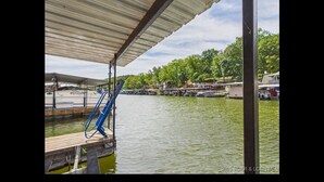A dock with a covered area, a boat ramp, and a view of a lake with boats and buildings in the background. - Cozy Lake House with a Private dock and beautiful outdoor space. (Rocky Mount)