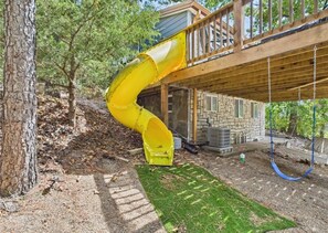 Un tobogán amarillo que se extiende desde una terraza de madera hacia un edificio de piedra.