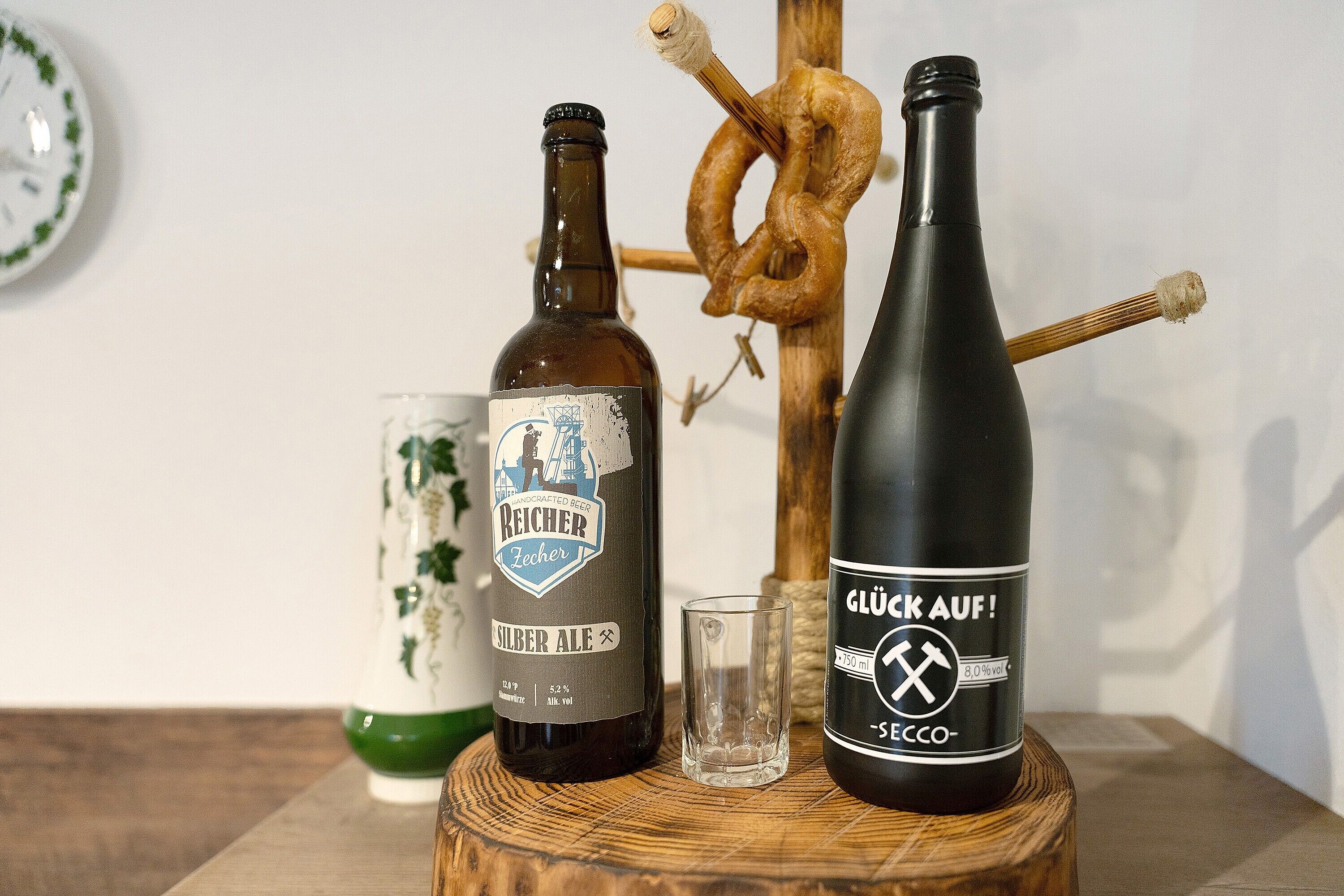 Twee flessen bier, een glas en een bretzel op een houten ondergrond.