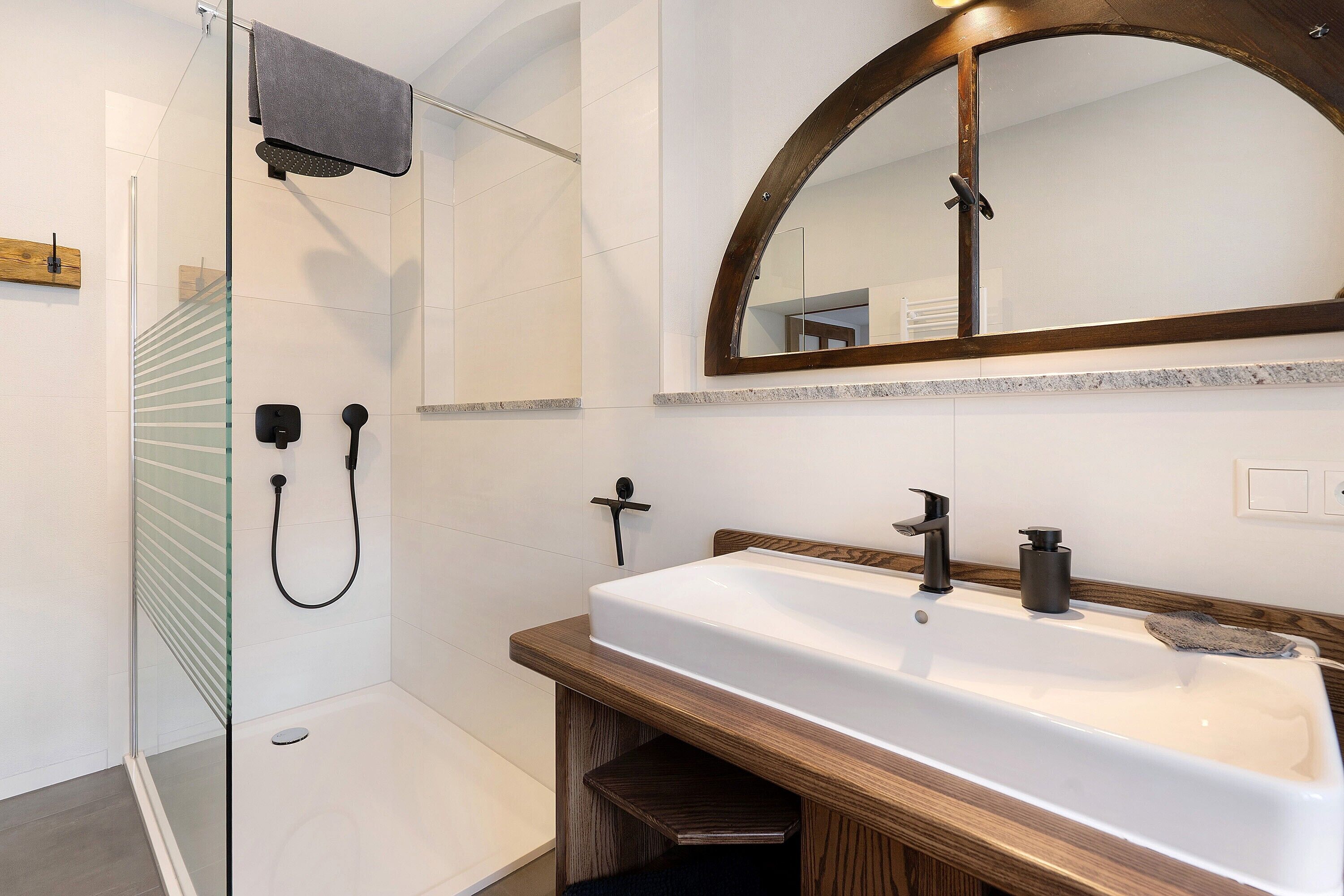 Een moderne badkamer met een douchecabine van glas, een houten wastafelmeubel, een grote spiegel en een witte wasbak.