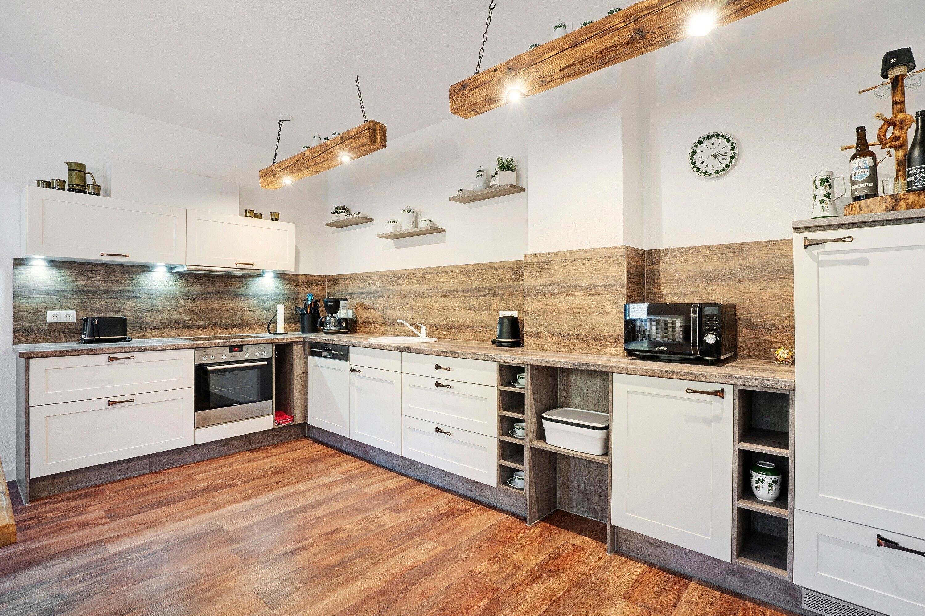 A modern kitchen with white cabinets, wooden flooring, and a built-in oven.