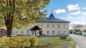 Suuri rakennus, jossa on huomiota herättävä torni, katettu sisäänkäynti ja asfaltoitu ajotie.