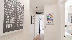 A hallway with a sign reading "ENTREPRENEUR DR." and a framed picture with the NBC logo and text "BUY THE NEWS SELL THE NEWS". - Wall Street Retreat - Modern , Luxury, Near Beach! (Port Orange)