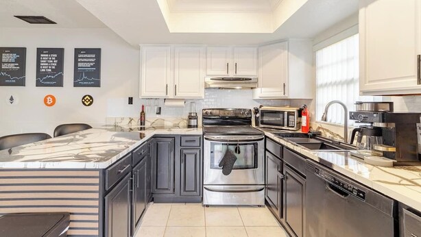 A modern kitchen with white cabinets, stainless steel appliances, and a marble countertop. - Wall Street Retreat - Modern , Luxury, Near Beach! (Port Orange)