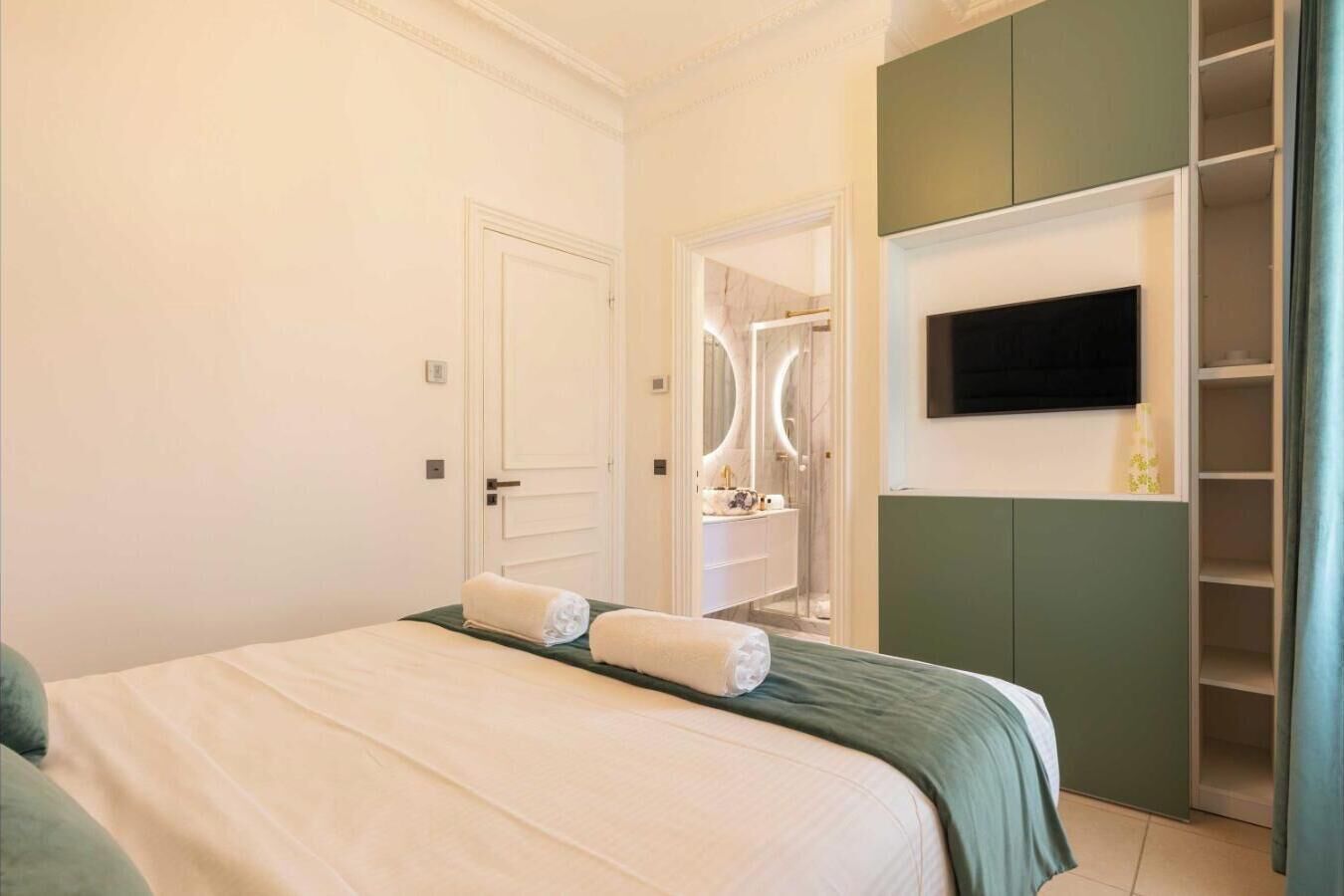 A hotel room with a bed, a TV mounted on the wall, a mirror, and a wardrobe.