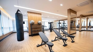 A modern gym with wooden flooring, black exercise benches, a punching bag, and various weightlifting equipment. - Studio completo Vl Olimpia Be my Guest (São Paulo)