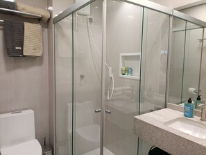 Une salle de bain moderne avec une douche à parois de verre, des toilettes blanches et un lavabo en granit agrémenté d’articles de toilette.