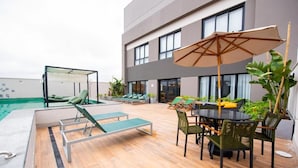 An outdoor pool area with lounge chairs, a table with chairs, and a large umbrella. - Studio completo Vl Olimpia Be my Guest (São Paulo)