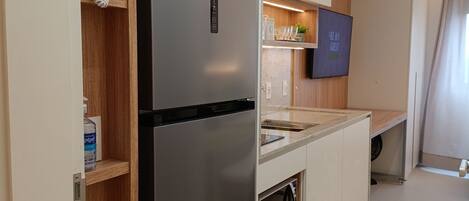 A modern kitchen with a stainless steel refrigerator, wooden shelves, a built-in oven, and a flat-screen TV on the wall.