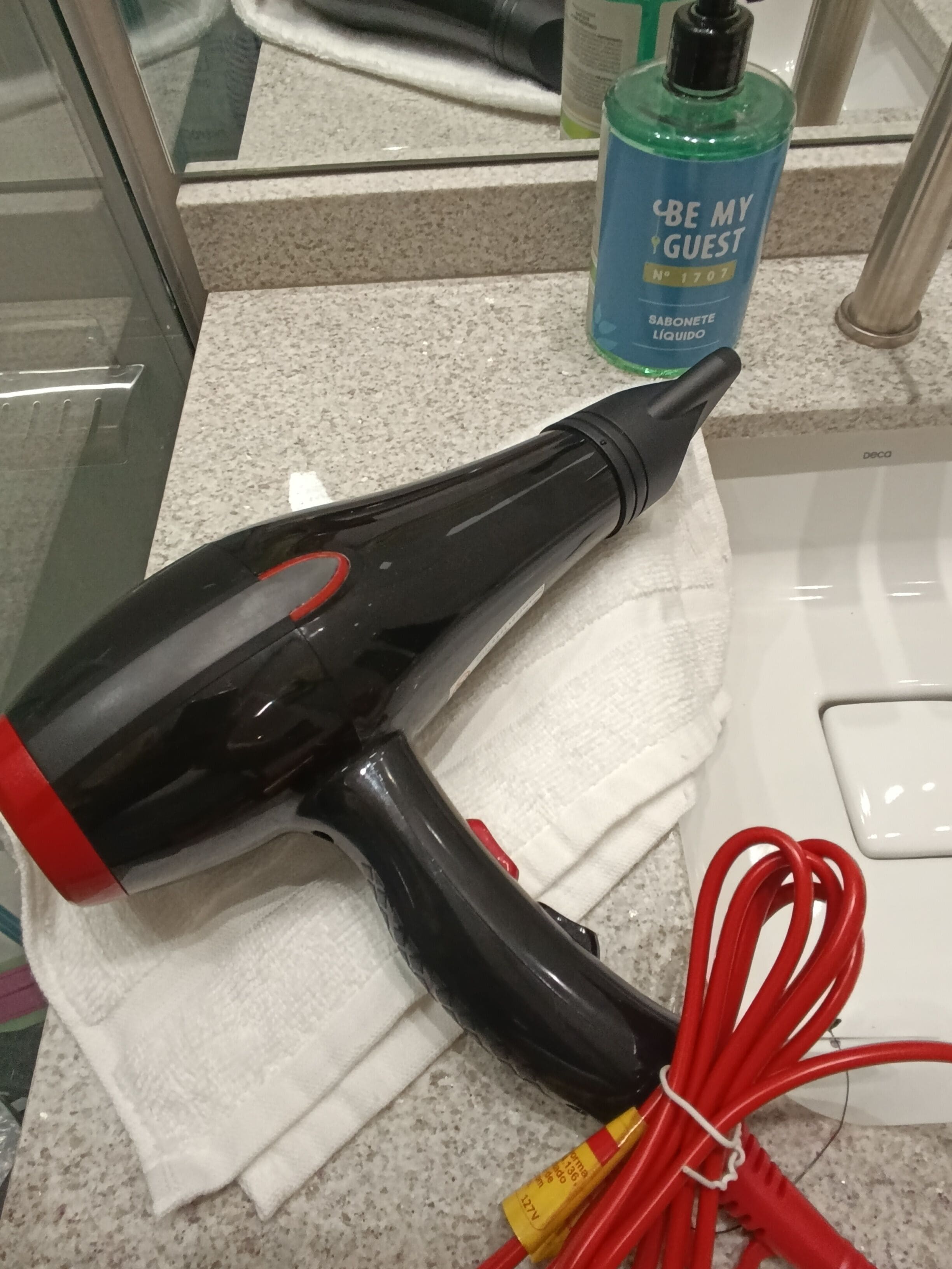 A bathroom with a towel, a hairdryer, and a bottle of hand soap on the counter.