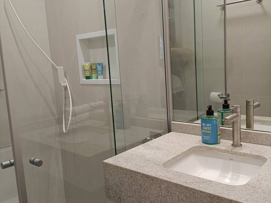 Une salle de bain moderne dotée d’une douche à parois de verre, d’un lavabo en granit et d’un miroir avec une étagère intégrée.