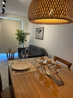 Un comedor con una mesa de madera dispuesta para dos personas, con un cuadro de un mapa mundial en la pared y una planta en maceta al fondo.