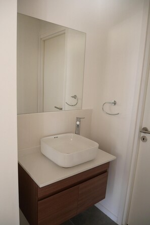 Un baño con un lavamanos blanco, un espejo y un perchero para toallas.