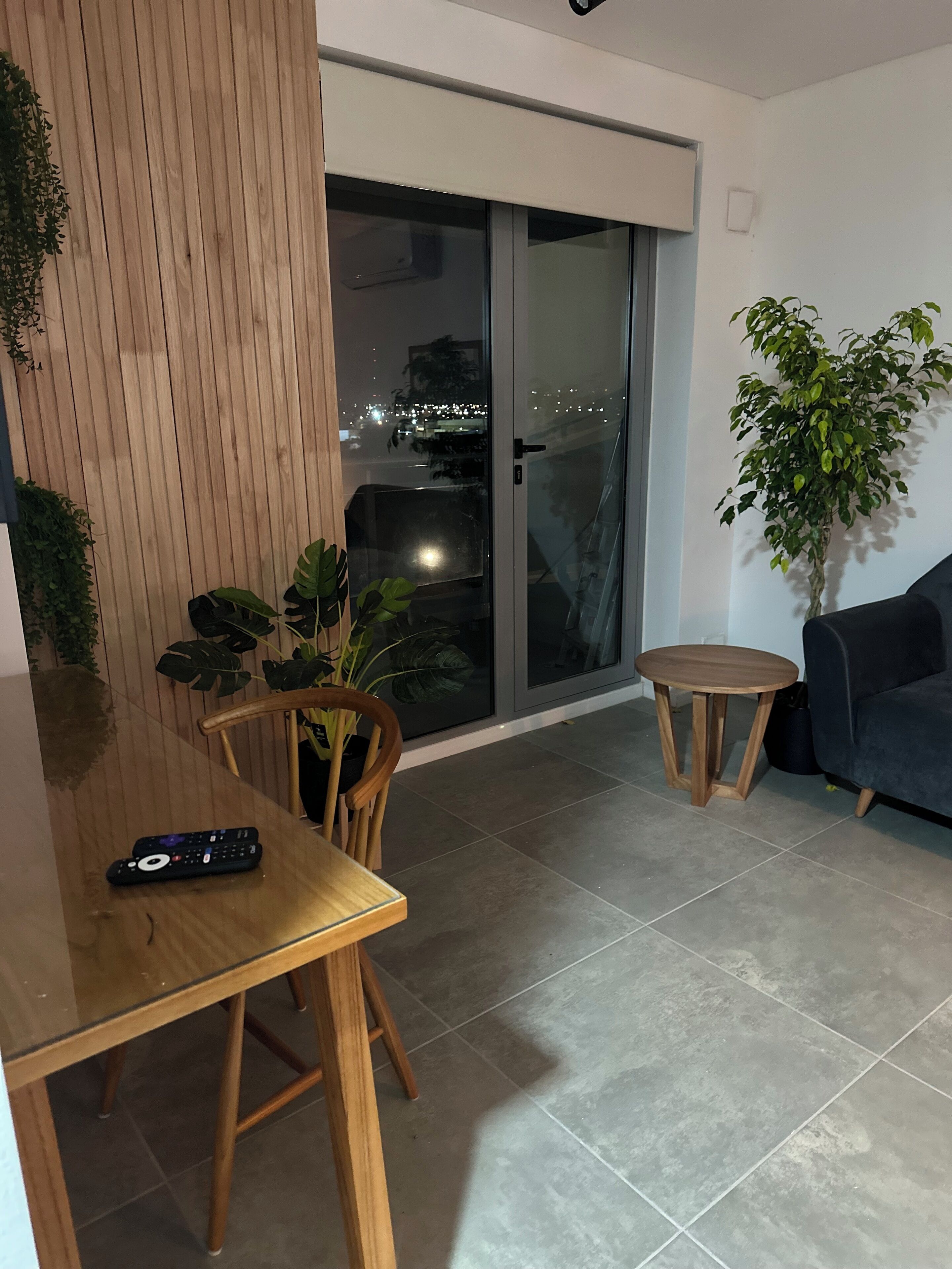 Una sala de estar moderna con una mesa de madera, dos sillas, un sofá oscuro y una planta en maceta.