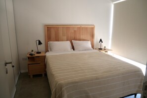 Un dormitorio con cabecera de madera, dos mesitas de noche, una cama con colcha a rayas y dos lámparas negras.