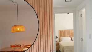Une chambre moderne avec un mur lambrissé en bois, un grand miroir rond, un luminaire suspendu, un lit soigneusement fait et une porte visible donnant sur une autre pièce.