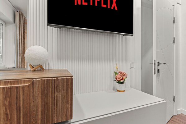 A modern bathroom with a wooden vanity, a white sink, and a wall-mounted TV displaying the Netflix logo.