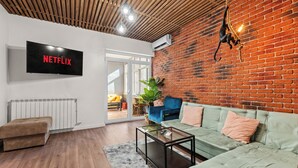 Een moderne woonkamer met een bakstenen muur, een groene bank, een bruin voetenbankje en een glazen salontafel.
