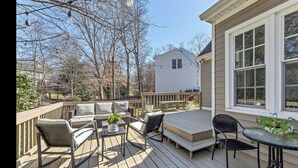 Una terraza de madera con mobiliario exterior, incluyendo un sofá, sillas y una mesa.