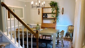 Un comedor con una mesa y sillas de madera, una araña y una planta en un estante.