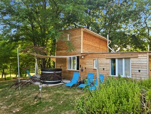 A wooden cabin with a hot tub, blue chairs, and a large tree in the background. - Gîte de la Liambe -wooden house in the countryside - sleeps 4 to 6 - (Dommartin-lès-Cuiseaux)