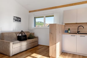 A compact living space with a sofa, a wooden cabinet, a window with a view, and a small kitchenette.