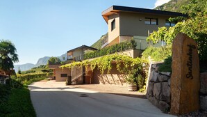 A modern building with a stone wall and a gate, surrounded by greenery and mountains.