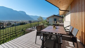 A terrace with a table and chairs, a wooden pergola, and a view of mountains and a vineyard.
