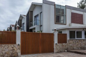 A modern multi-story residential building with a stone facade, large windows, and a wooden fence.