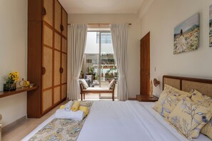 A bedroom with a bed, a wooden wardrobe, a bench, and a view of the outside.