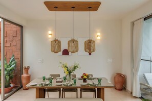 A dining area with a table set for four, a vase of flowers, and hanging light fixtures.