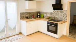 Et kompakt køkken med vask, komfur og ovn, hvide skabe og et mønstret backsplash.