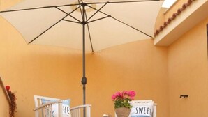 A room with a beige wall, a white chair, a table with a beige umbrella, and a sign that says "SWEET." - Sweet World - Family Room with Terrace Near the Beach (Terrasini)