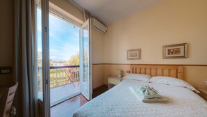 A hotel room with a large bed, a nightstand, a chair, a balcony with a table, and two framed pictures on the wall. - Inn Rome B&B  (Rome)
