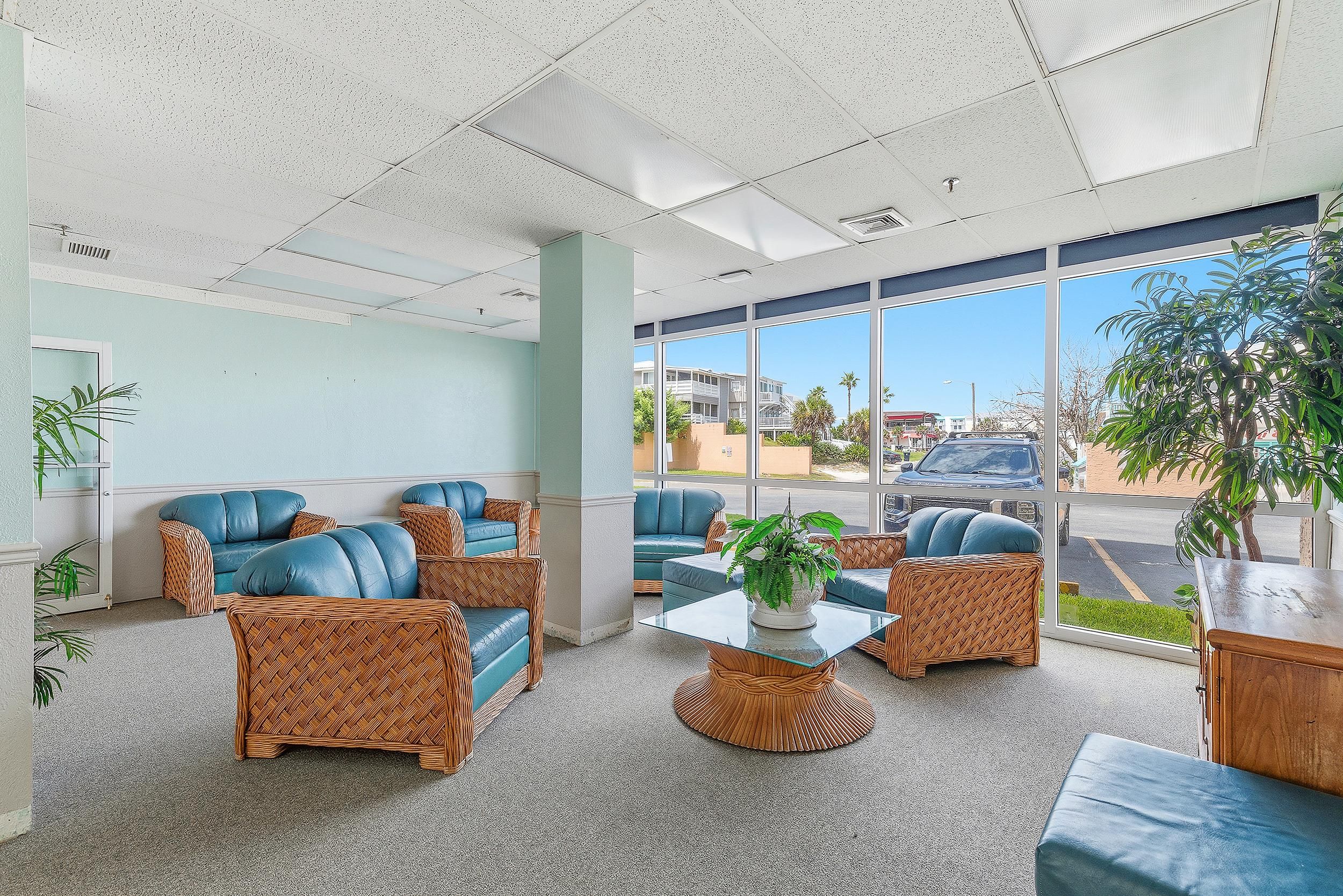 A spacious indoor area with wicker furniture, a glass coffee table, and large windows offering a view of the outside.