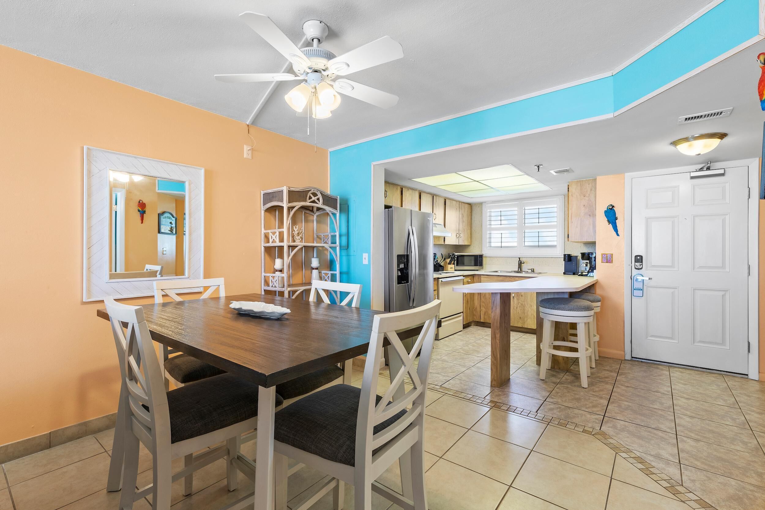 A dining area with a wooden table and chairs, a ceiling fan, and a kitchen area with cabinets and a refrigerator.