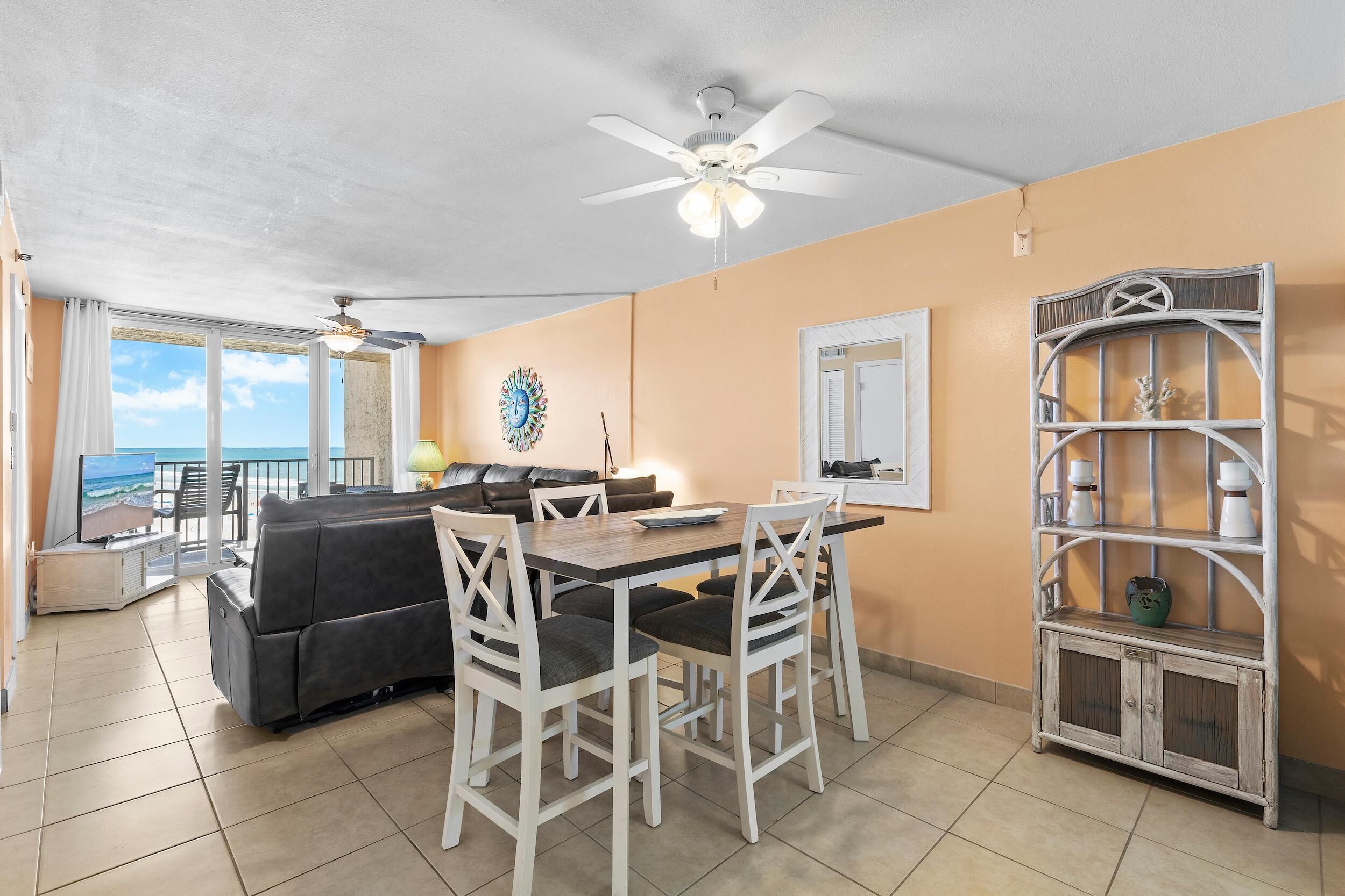 A dining area with a table and chairs, a ceiling fan, and a view of the ocean.