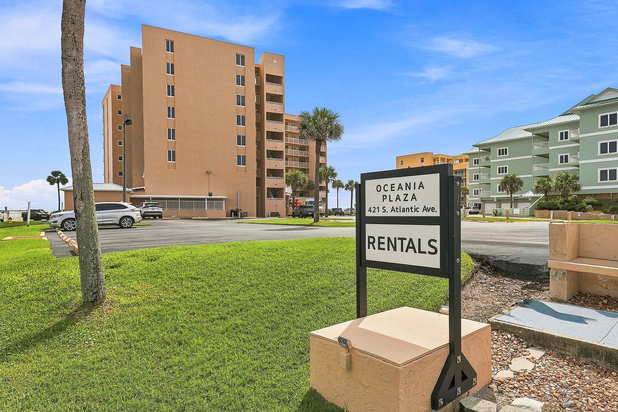 A sign for Oceania Plaza Rentals with a multi-story building in the background.