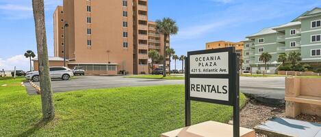 A sign for Oceania Plaza Rentals with a multi-story building in the background.