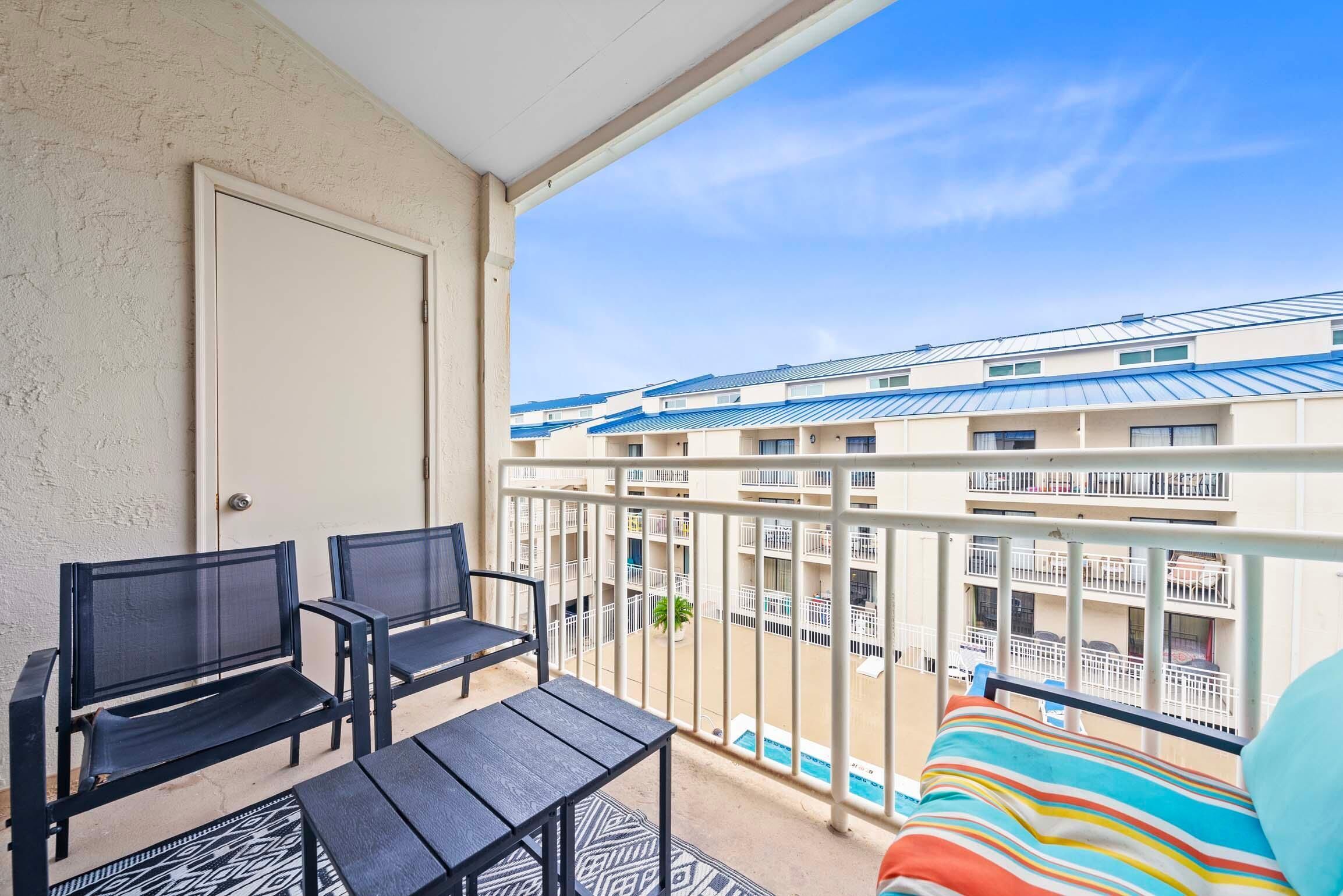A balcony with a view of a multi-story building, a door, and a bed with a striped blanket.
