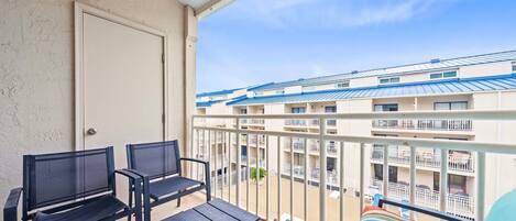 A balcony with a view of a multi-story building, a door, and a bed with a striped blanket.
