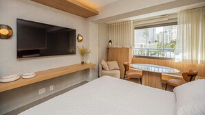A hotel room with a large bed, a TV mounted on the wall, a small table with chairs, and a window with curtains. - Flat c Piscina e Academia na Ch Cara Klabin (São Paulo)