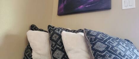 A brown leather sofa with patterned pillows against a beige wall, with a large abstract painting above.